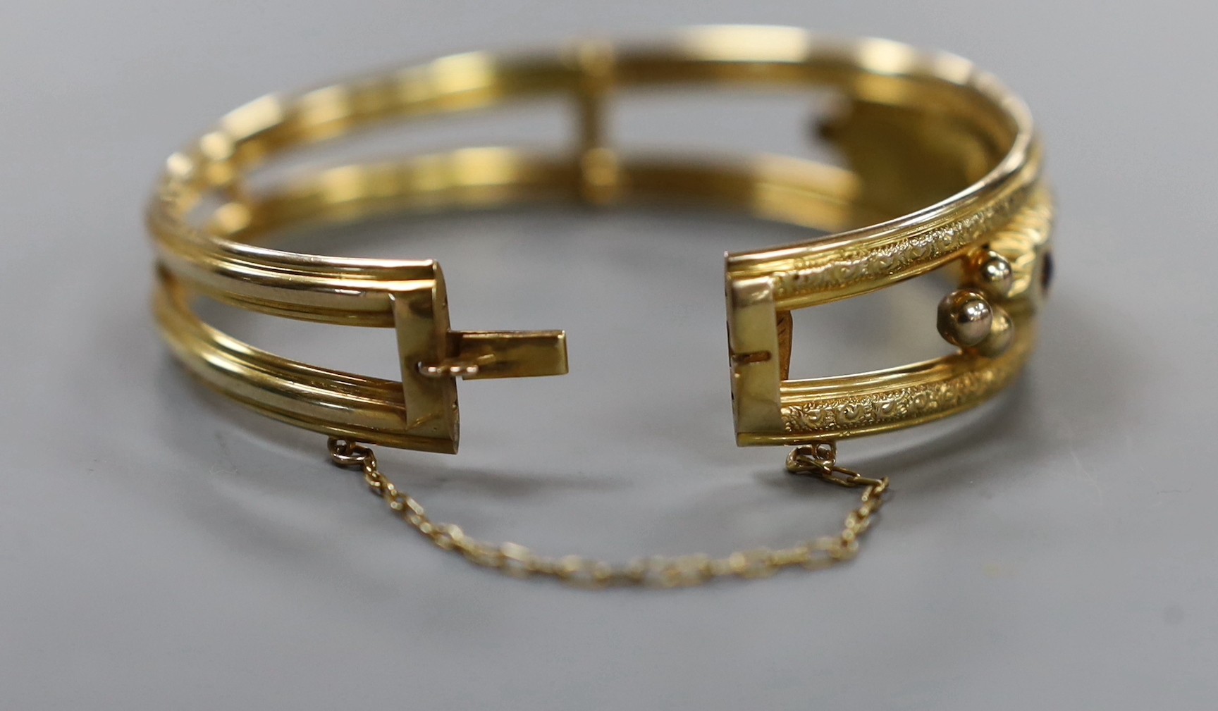 An Edwardian 9ct gold and three stone garnet and two stone diamond chip set hinged bangle, gross weight 12.5 grams.